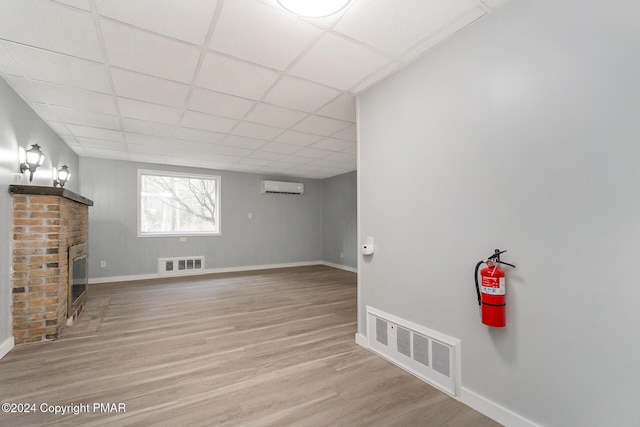 basement with a paneled ceiling, a wall mounted air conditioner, a fireplace, and visible vents