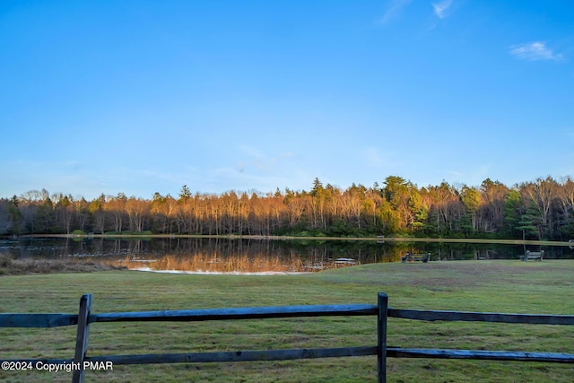 view of yard featuring a water view, fence, and a forest view