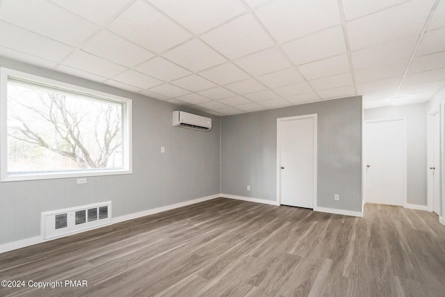 basement with a paneled ceiling, wood finished floors, visible vents, baseboards, and a wall mounted AC