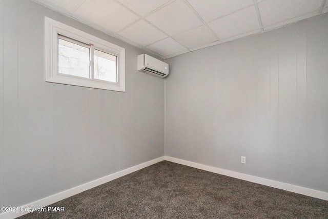 empty room featuring dark carpet, a drop ceiling, a wall mounted air conditioner, and baseboards