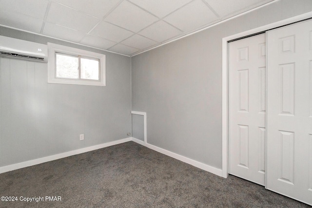 basement with a paneled ceiling, a wall mounted air conditioner, dark carpet, and baseboards