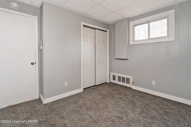 unfurnished bedroom with dark colored carpet, a paneled ceiling, a closet, and visible vents