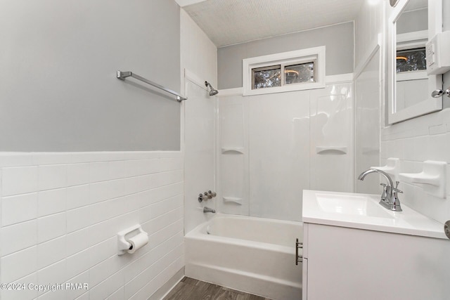 full bath with a wainscoted wall, shower / tub combination, wood finished floors, vanity, and tile walls