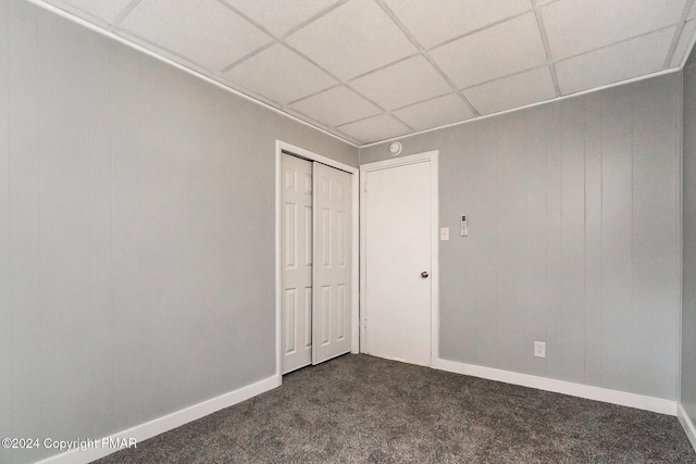 unfurnished bedroom with a paneled ceiling, baseboards, dark carpet, and a closet