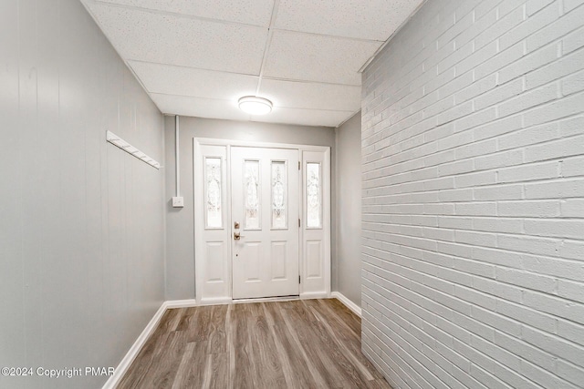 foyer featuring brick wall, baseboards, a drop ceiling, and wood finished floors