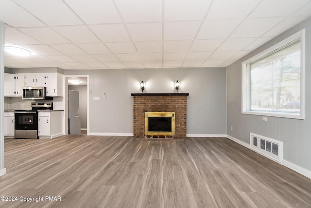 unfurnished living room featuring light wood-style flooring, a brick fireplace, visible vents, and baseboards