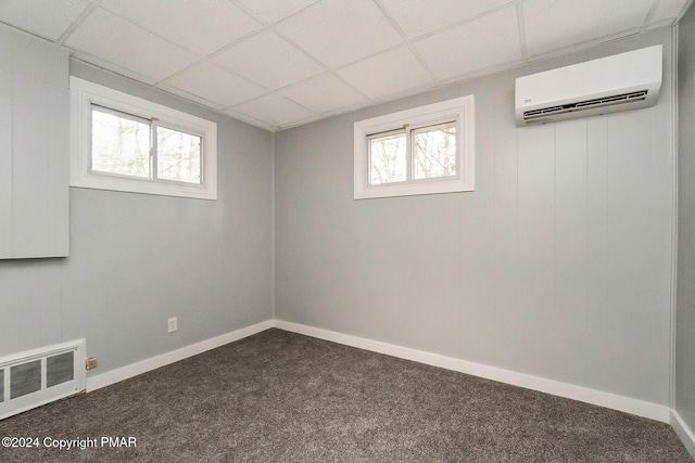 below grade area with a drop ceiling, visible vents, baseboards, a wall mounted AC, and dark carpet