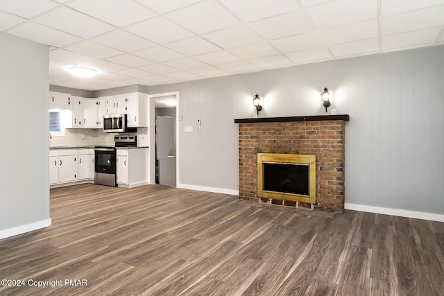 unfurnished living room featuring a brick fireplace, dark wood finished floors, and baseboards