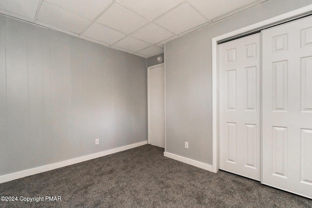 unfurnished bedroom with baseboards, a closet, dark carpet, and a drop ceiling