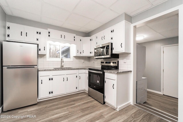 kitchen featuring decorative backsplash, white cabinets, appliances with stainless steel finishes, light wood-type flooring, and a sink