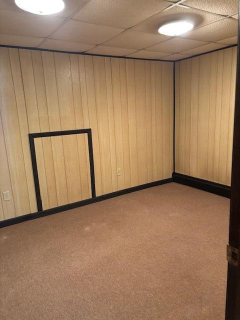 carpeted empty room featuring wood walls and a drop ceiling