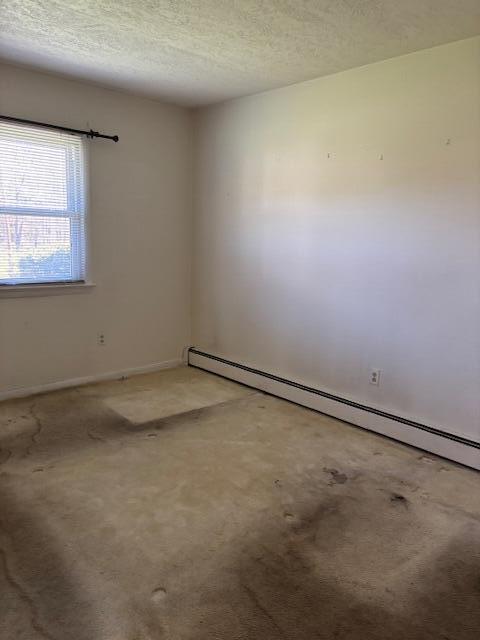 empty room with light colored carpet, a baseboard radiator, a textured ceiling, and baseboards