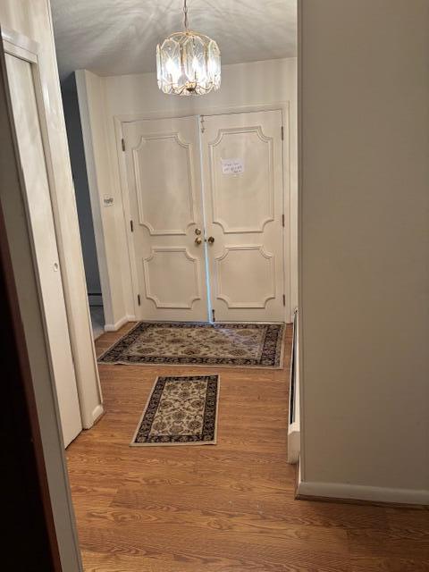 doorway to outside with baseboards, wood finished floors, and a notable chandelier