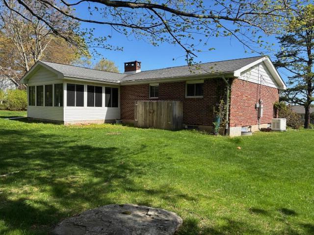 rear view of house featuring a sunroom, central AC, a yard, and a chimney