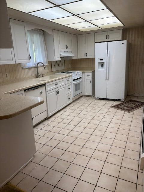 kitchen with light countertops, under cabinet range hood, white appliances, and a sink