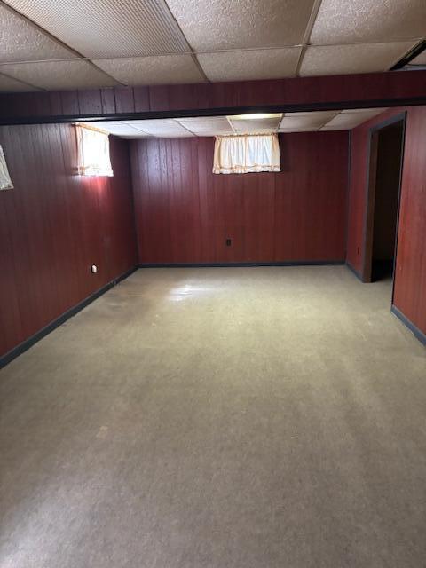 basement with a drop ceiling and wooden walls