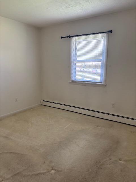 empty room featuring light colored carpet, baseboards, and a baseboard heating unit