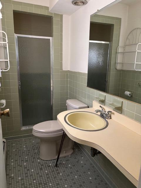 bathroom with tile patterned floors, a shower stall, toilet, and tile walls