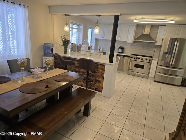 kitchen with wall chimney range hood, light tile patterned floors, stainless steel appliances, and light countertops