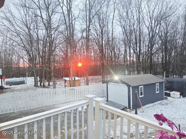 yard covered in snow featuring a fenced front yard, an outdoor structure, and a detached garage