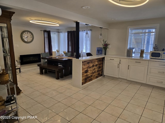 kitchen featuring light countertops, white microwave, white cabinetry, light tile patterned flooring, and a peninsula