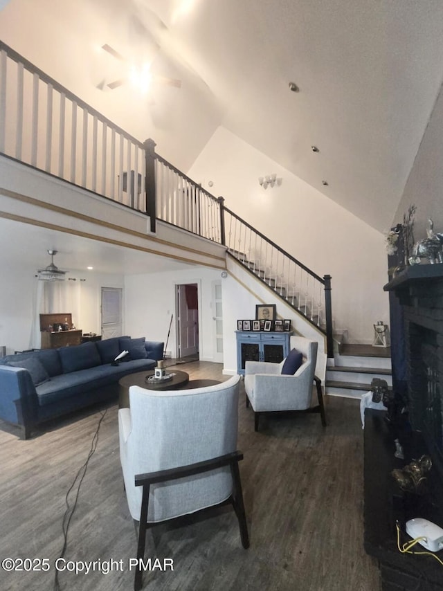 living area with high vaulted ceiling, a fireplace, wood finished floors, a ceiling fan, and stairway