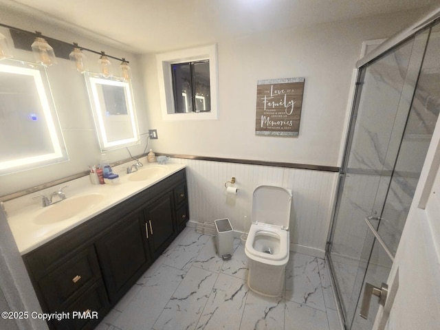 bathroom with marble finish floor, a stall shower, a sink, and wainscoting