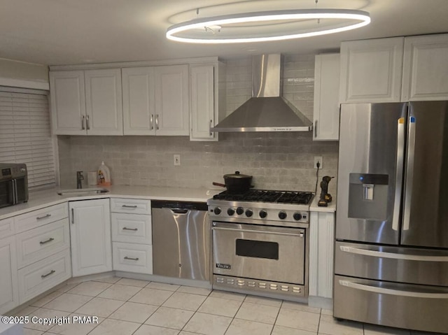 kitchen with light tile patterned floors, stainless steel appliances, light countertops, backsplash, and wall chimney exhaust hood