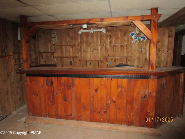 bar with a bar, wood walls, and a drop ceiling