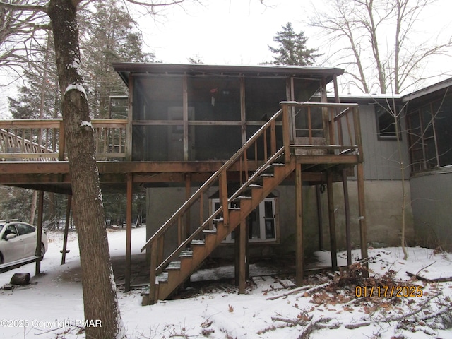 snow covered back of property with stairway and a sunroom