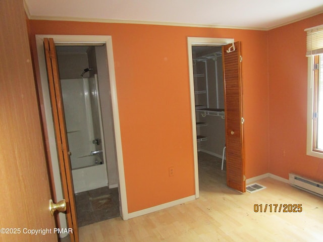 unfurnished bedroom featuring a walk in closet, a closet, visible vents, baseboard heating, and wood finished floors