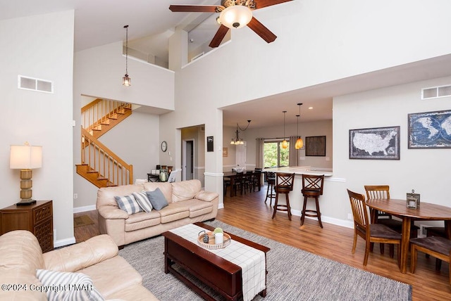 living area with ceiling fan with notable chandelier, stairway, wood finished floors, and visible vents