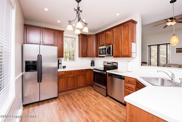 kitchen with brown cabinets, hanging light fixtures, stainless steel appliances, light wood-style floors, and a sink