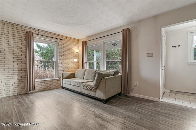 living room featuring brick wall, baseboards, and wood finished floors