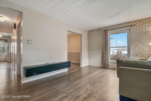 living room with brick wall, a textured ceiling, baseboards, and wood finished floors