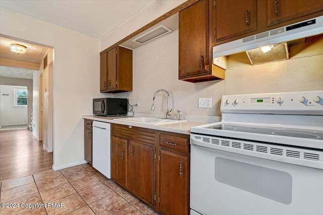 kitchen with white appliances, light tile patterned floors, light countertops, under cabinet range hood, and a sink