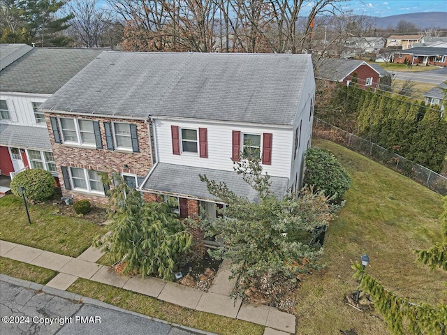 view of front facade with brick siding, fence, a front lawn, and roof with shingles