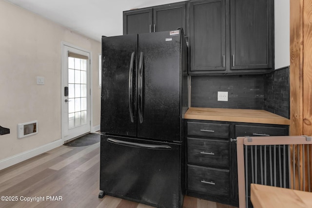 kitchen featuring wood counters, dark cabinetry, freestanding refrigerator, light wood finished floors, and tasteful backsplash