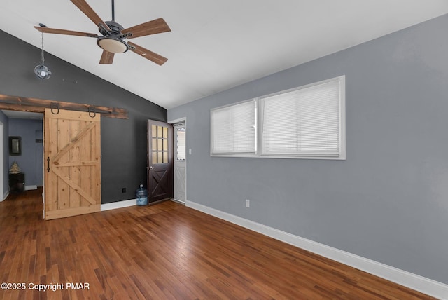 unfurnished living room with a barn door, baseboards, a ceiling fan, wood finished floors, and vaulted ceiling