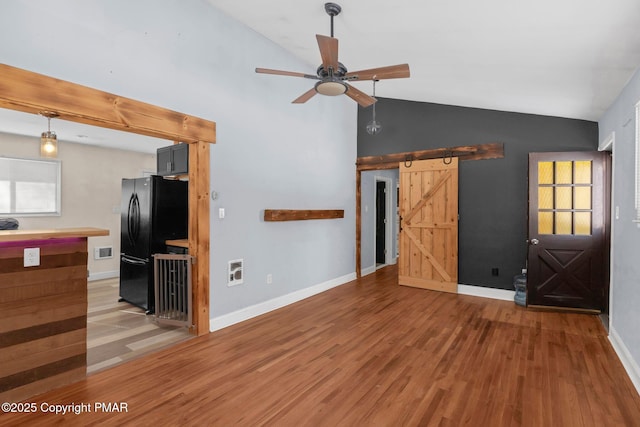 unfurnished living room featuring ceiling fan, a barn door, hardwood / wood-style floors, and a wealth of natural light