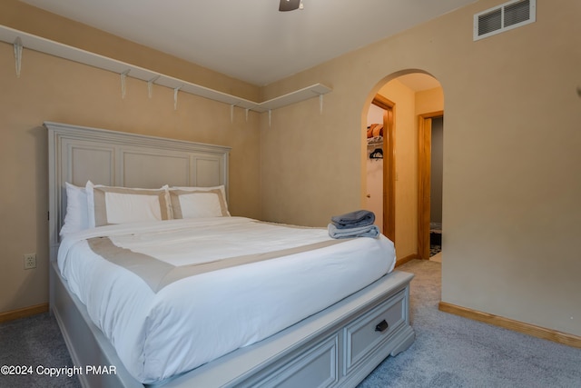 bedroom with light colored carpet, arched walkways, visible vents, and baseboards