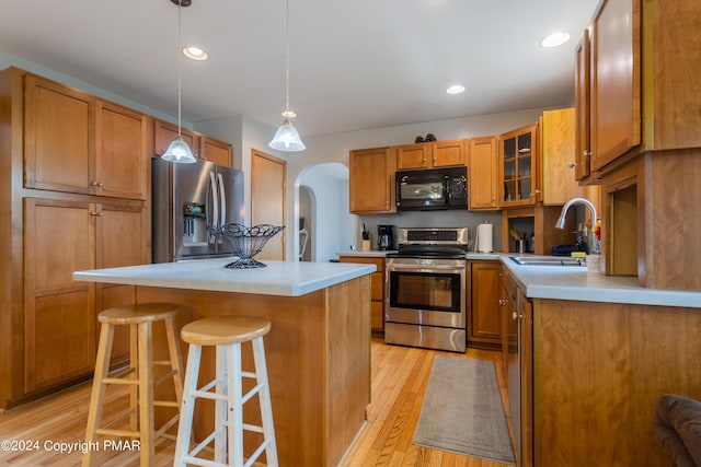 kitchen featuring light wood finished floors, arched walkways, a breakfast bar area, stainless steel appliances, and a sink