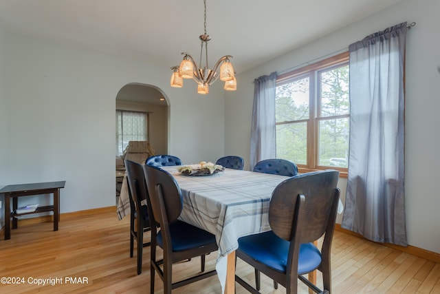 dining area featuring a chandelier, arched walkways, baseboards, and light wood finished floors