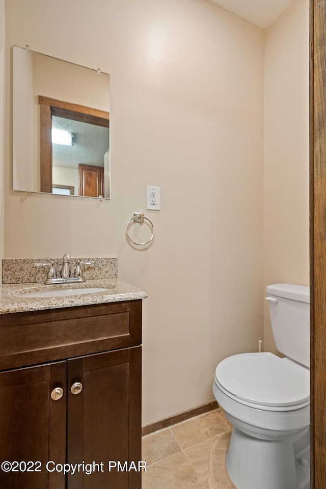 half bath with baseboards, vanity, and toilet