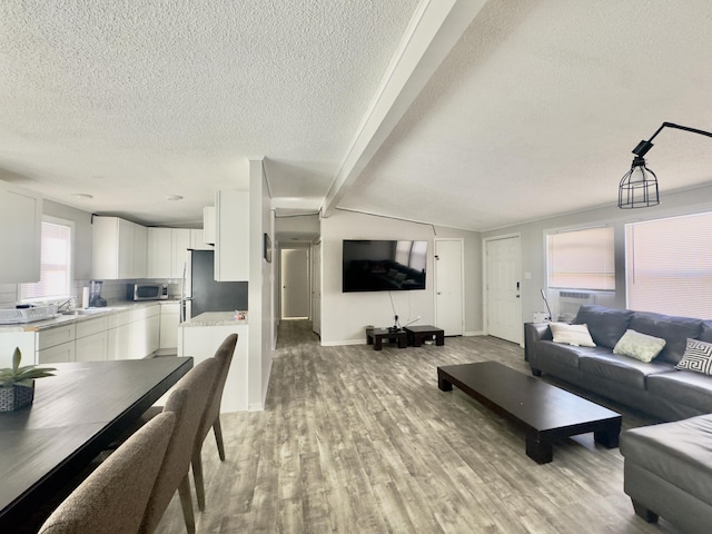 living area featuring beamed ceiling, light wood-style floors, cooling unit, and a textured ceiling