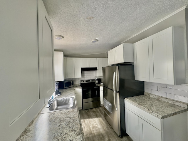 kitchen featuring wood finished floors, a sink, stainless steel appliances, white cabinets, and backsplash