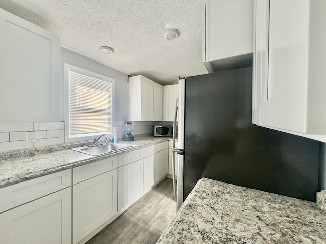 kitchen featuring tasteful backsplash, light wood finished floors, appliances with stainless steel finishes, white cabinetry, and a sink