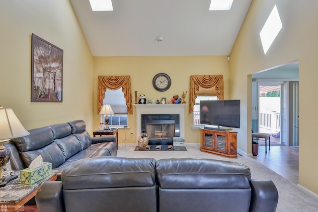 living area with a fireplace with flush hearth, carpet flooring, a skylight, high vaulted ceiling, and baseboards