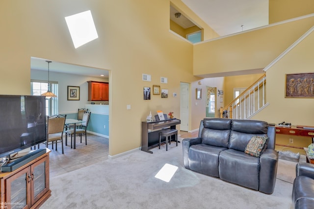 living room with a high ceiling, stairway, a skylight, light carpet, and baseboards