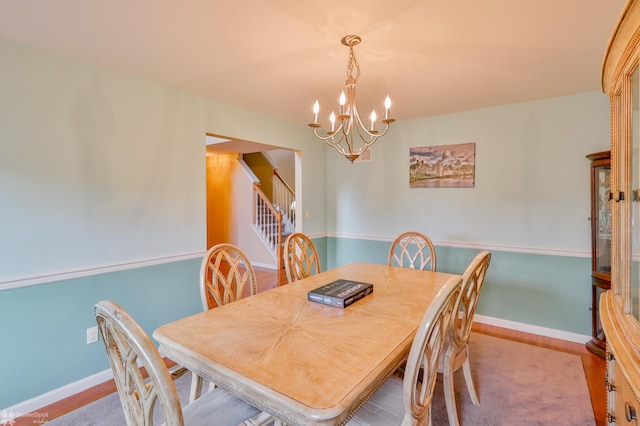 dining area featuring a chandelier, stairs, baseboards, and wood finished floors